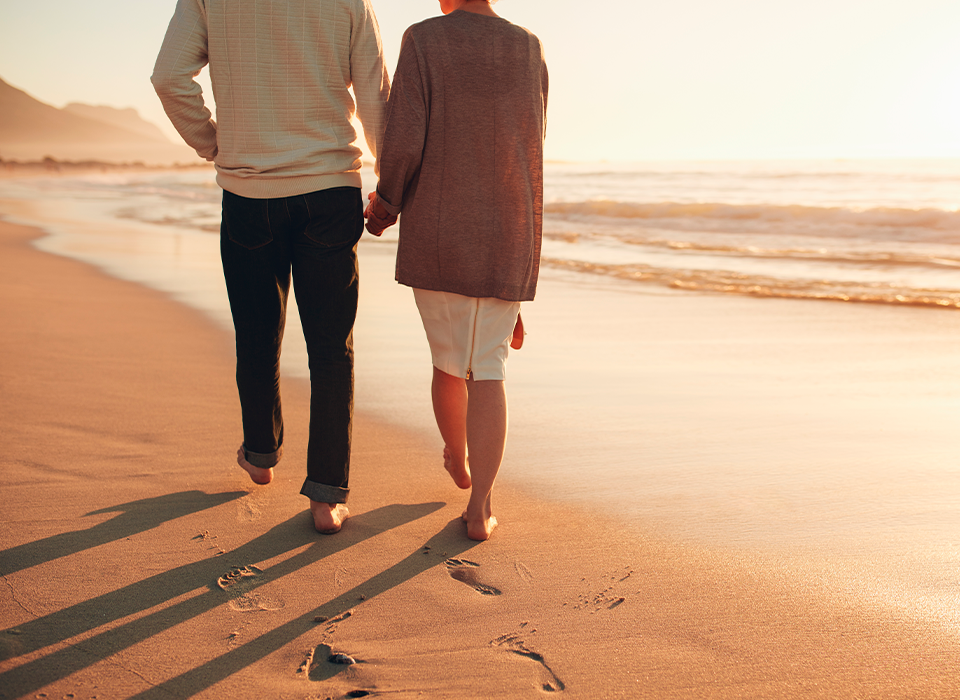 Senior couple holding hands walking on the beach enjoying the sunset.